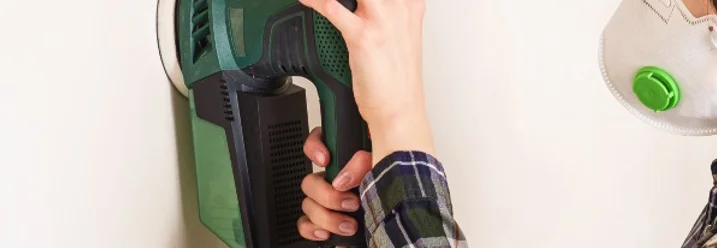 Person schleift Wand mit Schleifmaschine